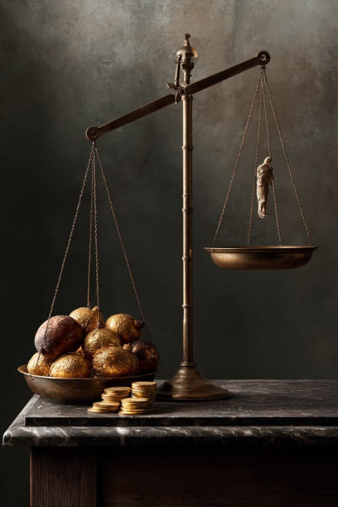 Antieke weegschaal in disbalans: goud en verguld fruit wegen zwaar, terwijl een klein, kwetsbaar figuurtje machteloos wordt opgetild — beeld bij het essay over morele volwassenheid.